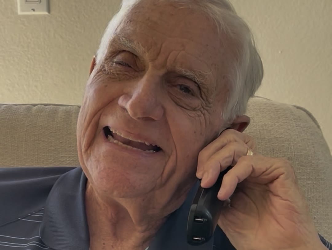 Nick's grandpa laughing with a phone to his ear, on a call with Donna